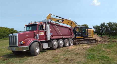 Red dump trucking being filled by an excavator